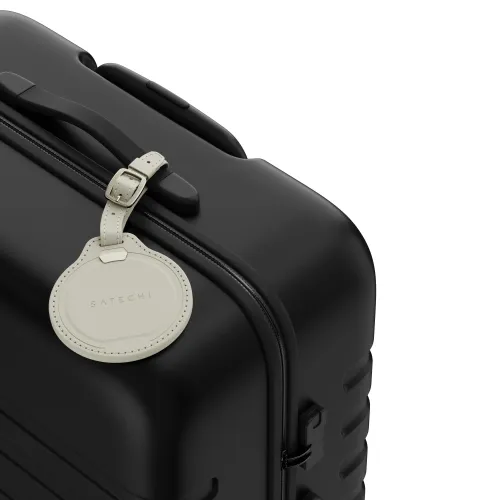 Sandfarget Satechi-bagasjelapp i vegansk skinn, rund med stropp og spenne, festet til svart koffert; SATECHI-logo synlig.