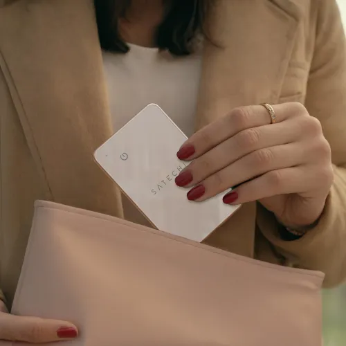 "Satechi FindAll" dykumos rausvos spalvos plonos kreditinės kortelės formato su užapvalintais kampais ir maitinimo piktograma, įdedama į ryškiai rožinę rankinę.