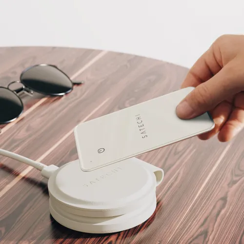 "Satechi FindAll" piniginės kortelė, laikoma virš baltos įkrovimo plokštelės ant medinio stalo, itin plona kortelė su logotipu; šalia - akiniai nuo saulės.