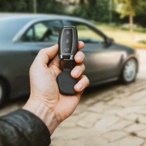 "Satechi FindAll" raktų pakabukas iš juodos veganiškos odos, kvadratinis dėklas ant dirželio ir žiedo, čia stambiu planu laikomas rankoje su automobilio raktu.