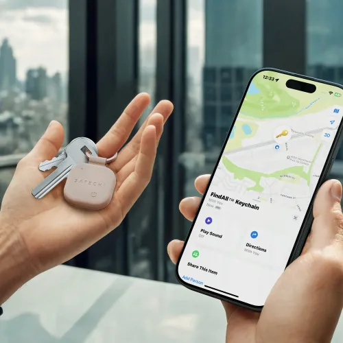 "Satechi Findall" raktų pakabukas iš dykumos rausvos veganiškos odos, pritvirtintas prie raktų, šalia "iPhone", kuriame rodomas žemėlapio vaizdas "Find My key".