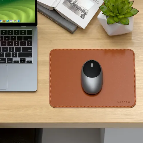 Musematte i brunt vegansk skinn med avrundede hjørner og sømmer, SATECHI-logo nederst til høyre, med musen på toppen på skrivebordet.