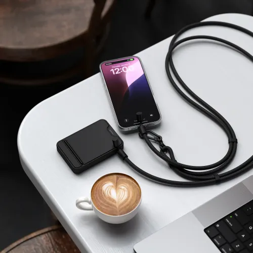 Satechi OntheGo Crossbody Lanyard Cable i svart, flettet stropp med karabinkrok på bordet, koblet til smarttelefon og powerbank.