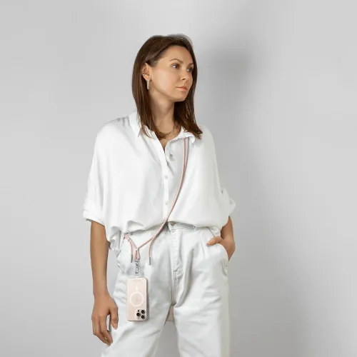 Ökenrosa crossbody-nyckelband med metallkontakter och karbinhake, bärs över axeln och håller en telefon hängande vid höften.