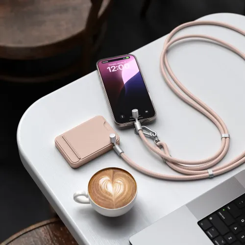 Crossbody-lanyard med flätad laddningskabel i ökenrosa, med karbinhake och metallhylsor ansluten till mobil på bord.