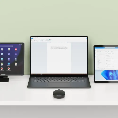 Satechi OntheGo Bluetooth-mus på et skrivebord ved siden af en laptop og to tablets til brug med flere enheder