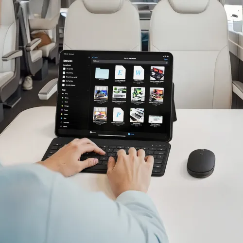 Satechi OntheGo trådlös mus bredvid ett iPad-tangentbordsfodral i en flygplanskabin