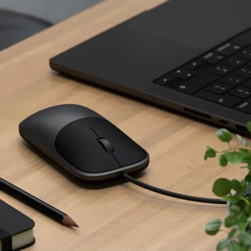 Satechi Slim LX trådad mus i rymdsvart med scrollhjul och kabel på ett skrivbord bredvid en bärbar dator.
