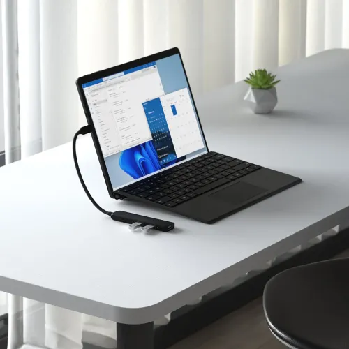 USB-C 4-in-1 slim multiport adapter in black with braided cable, connected to laptop; two USB-A devices plugged in, on the table.