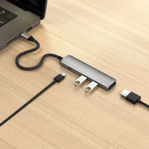 USB-C multiportadapter i rymdgrå på skrivbord, ansluten till laptop; två USB-minnen isatta, synlig USB‑C‑port och HDMI‑ände.