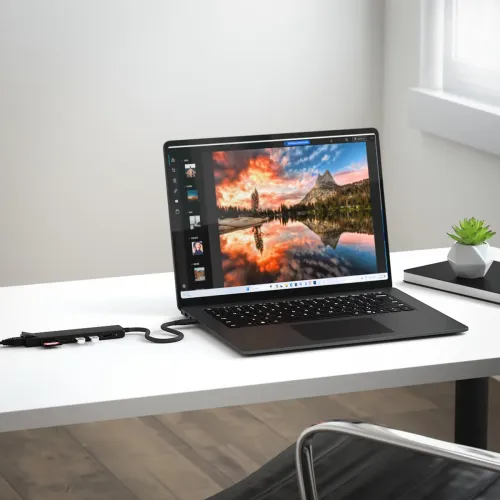 Satechi USB-C 7-in-1 daudzvadu adapteris melnā krāsā uz darbvirsmas, pievienots klēpjdatoram; redzams HDMI ports un pievienoti divi USB-A.