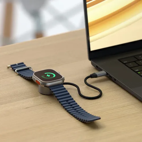 USB‑C magnetisk laddkabel för Apple Watch laddar klockan på puck, ansluten med kort flätad kabel till laptopens USB‑C‑port.