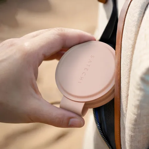 Satechi OntheGo 2-i-1 trådløs lader i Desert Rose, rund og brettet med stroppsløyfe, holdes i den ytre lommeåpningen på en veske.