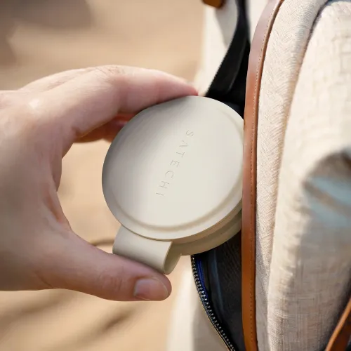 Satechi OntheGo trådløs lader i sand, rund og sammenleggbar, holdes i én hånd og senkes ned i en liten lomme på en tøypose.
