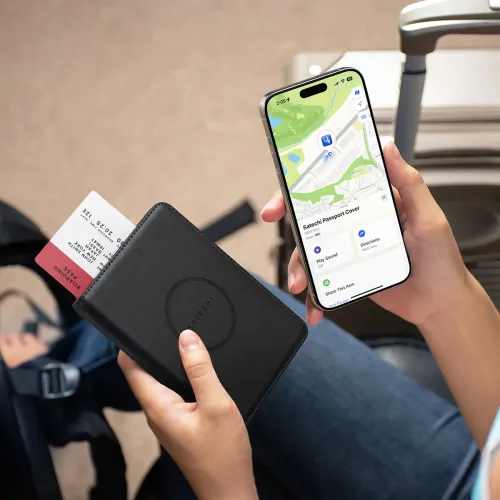 Satechi passetui i svart lær holdes i hånden med boardingkortet delvis satt inn, ved siden av iPhone som viser Find My map-skjermen.